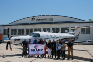 Western Aircraft employees stand outside building with SHARP award flag