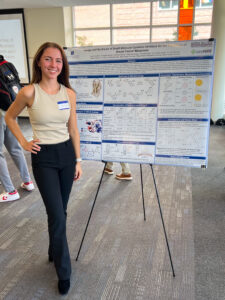 Lauren Snider standing in front of her presentation board on small molecule inhibitors.