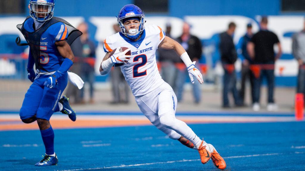 Boise State football player carries a ball in arm as he sprints across the blue.