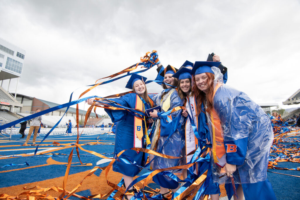 Boise State graduates pose on the Blue Turf with confetti in hand.