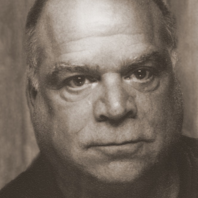 A black and white photo of a round-faced white man who looks directly into the camera