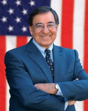 Leon Panetta standing in front of an American Flag, smiling with arms crossed