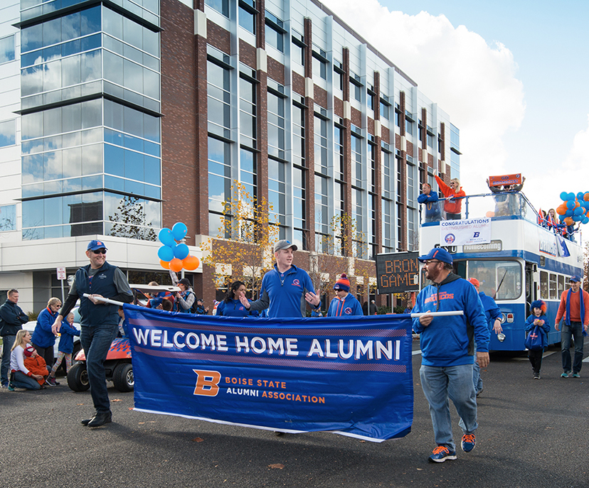 Alumni members walk in parade holder banner that says Welcome Home Alumni