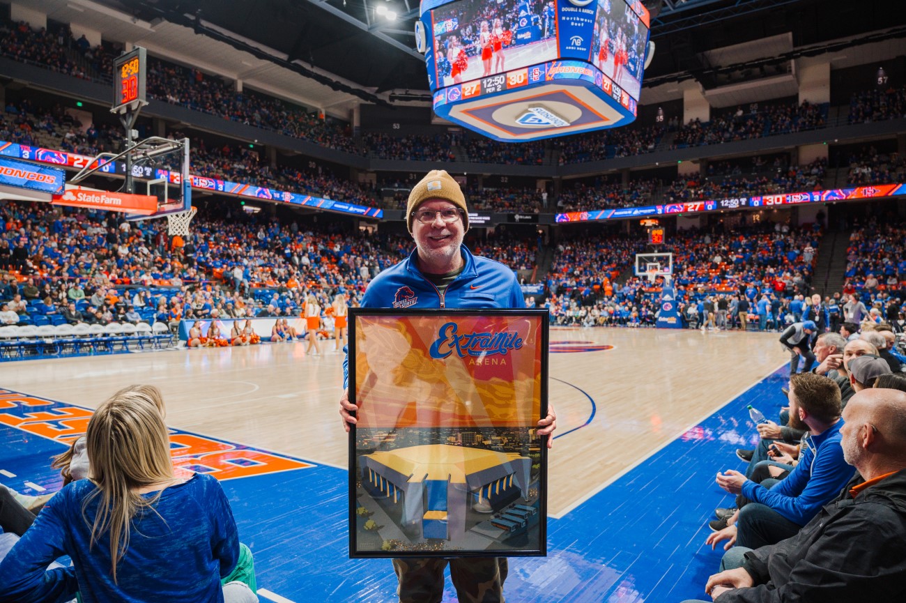 Ward Hooper showcasing framed poster at ExtraMile Arena during a basketball game