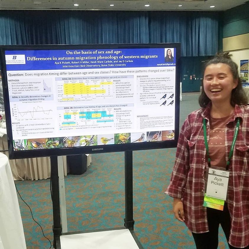a female undergraduate student stands smiling next to her research poster which displays a number of graphs and small text