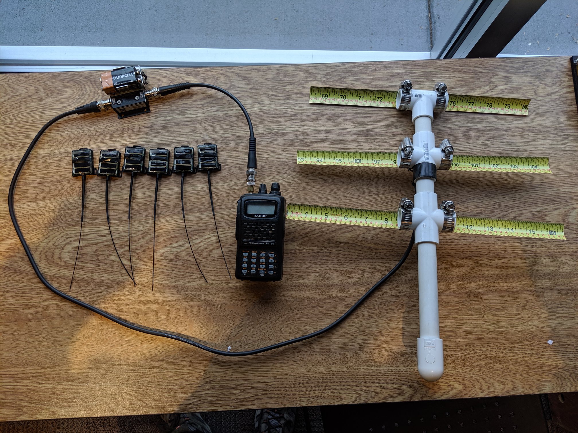 six small transmitters with antennas sit on a desk with a larger t-shaped receiver antenna