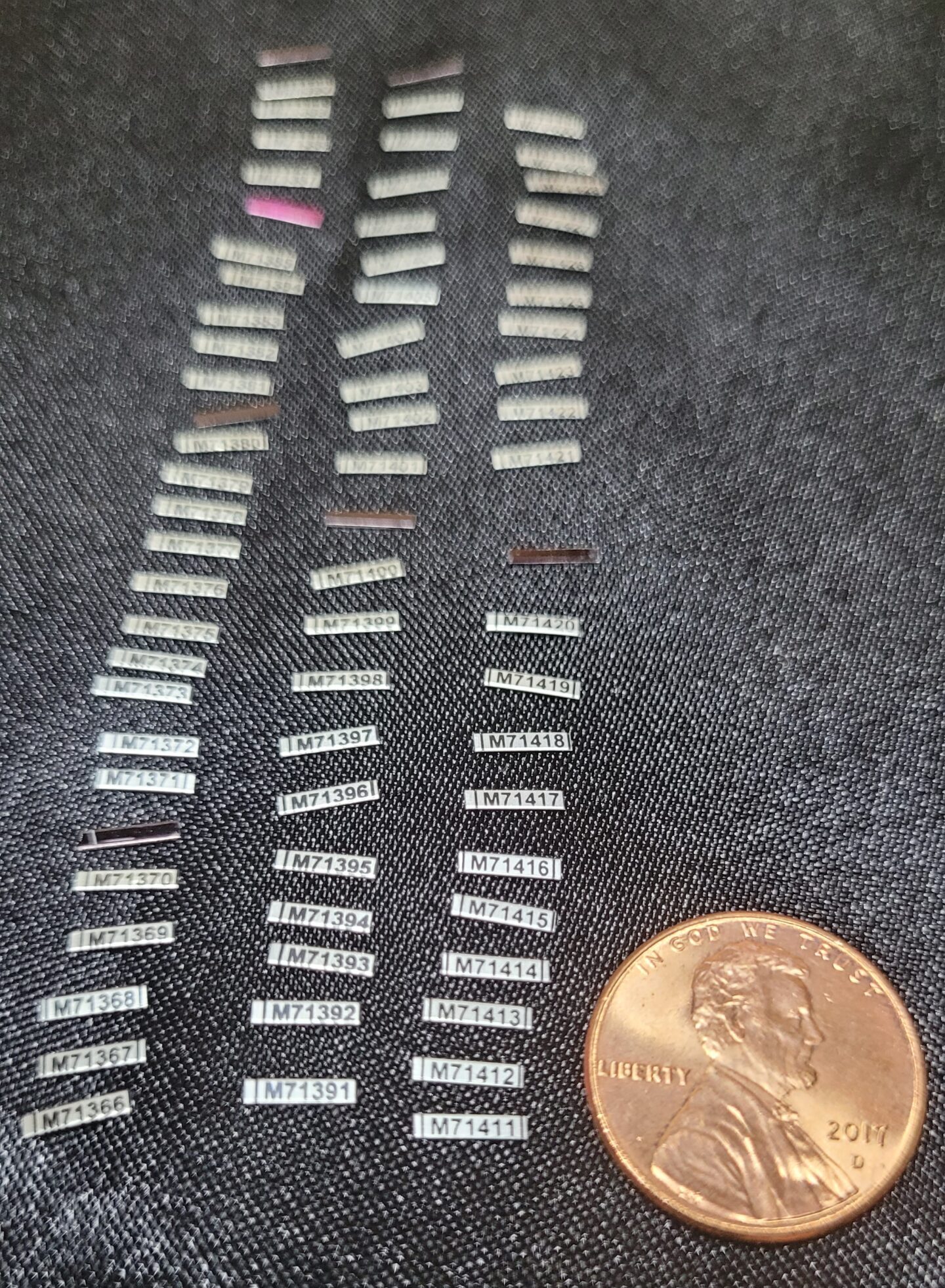 about seventy flat, unformed hummingbird bands laid out on a table. A penny for scale shows each band is about the length of Abraham Lincoln's head. The numbers on the band are about the size of the year stamped on the penny