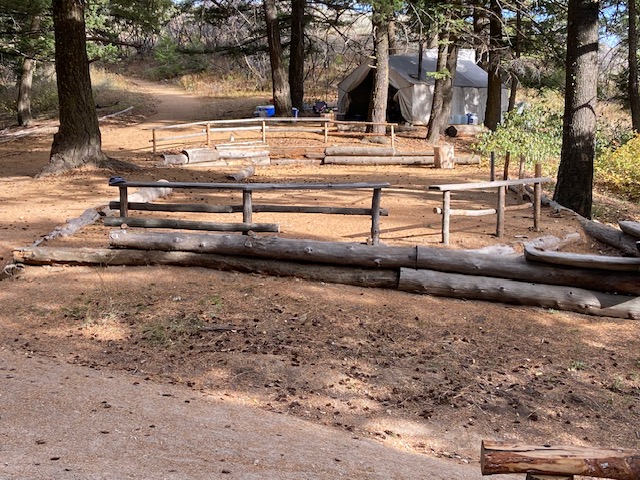 a view of Lucky Peak's main camping pad, with the large kitchen wall tent in the background. Around the edge of the camping area are freshly built railings made from douglas fir logs