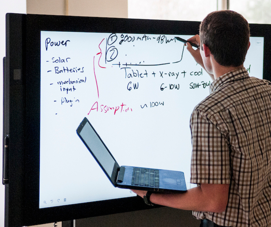 Student standing in front of digital whiteboard as they transfer over notes from their computer screen