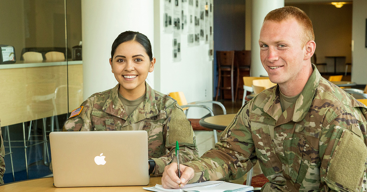 Two military students work on a laptop at a table