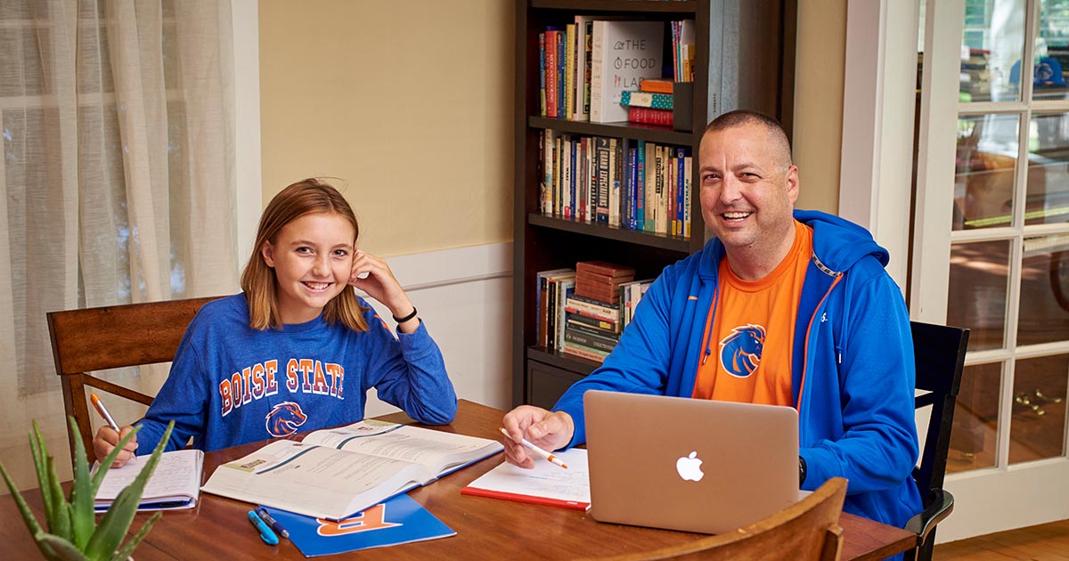 Father and daughter sitting side by side and working on school work together