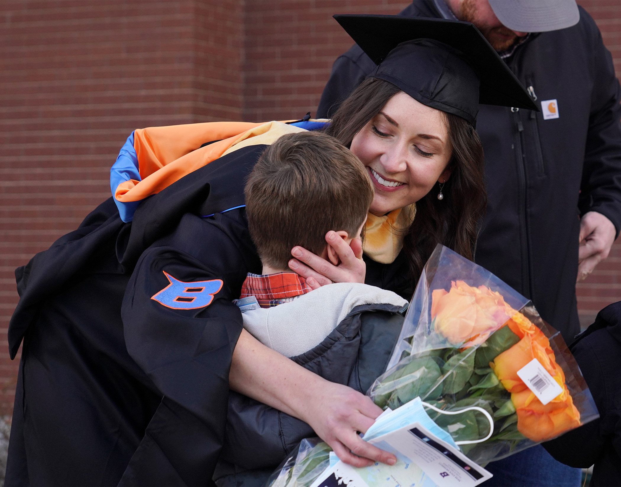A graduate in a cap and gown hugs her child. 