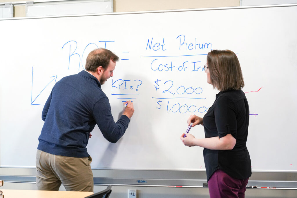 Two MBA students brainstorm on a whiteboard