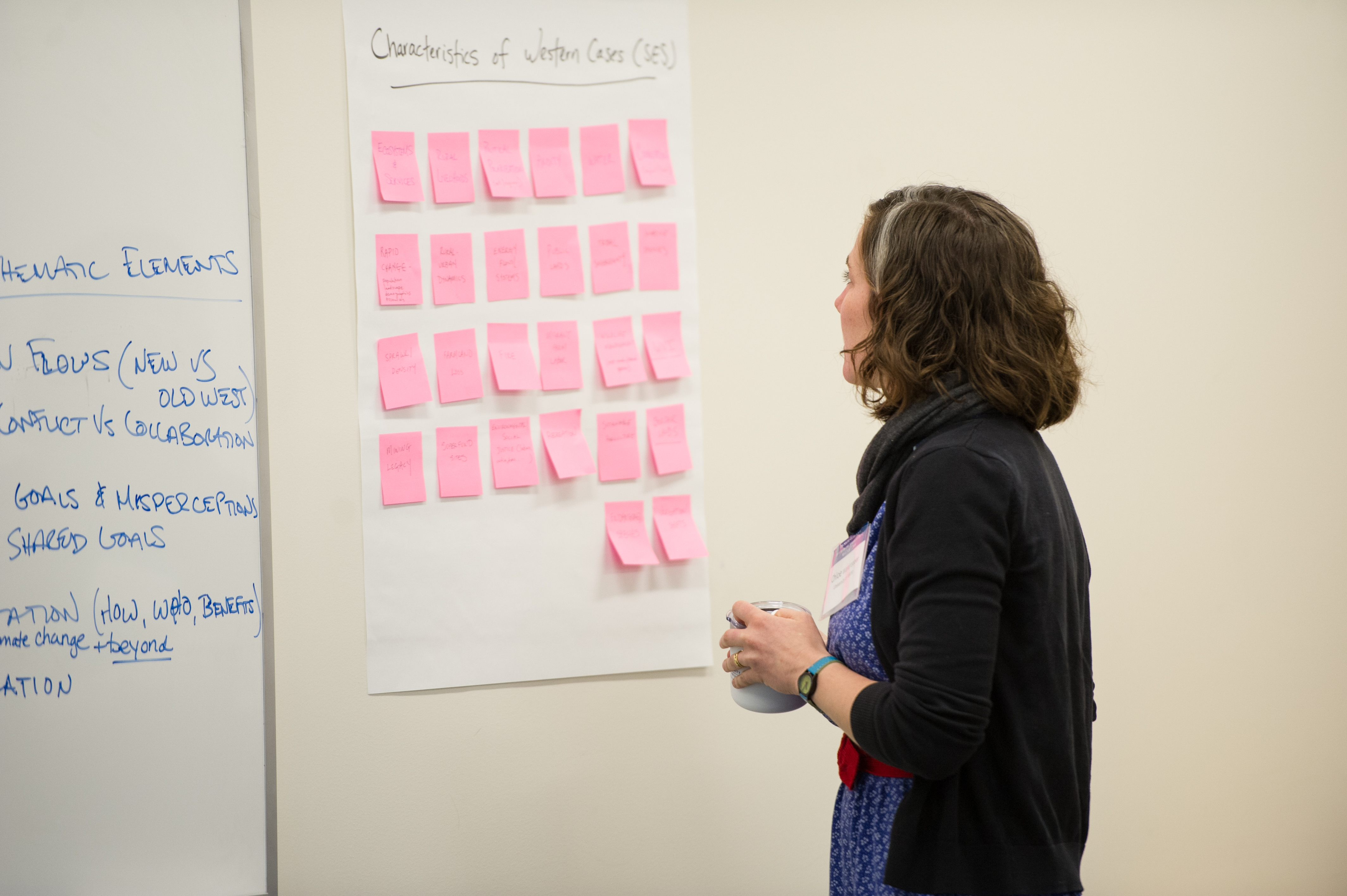 One woman looking at paper stuck to wall that has a grid of colored sticky notes