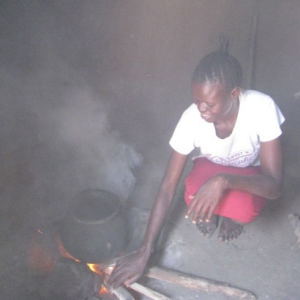 Kenyan woman using a cooking pot over n open wood burning fire