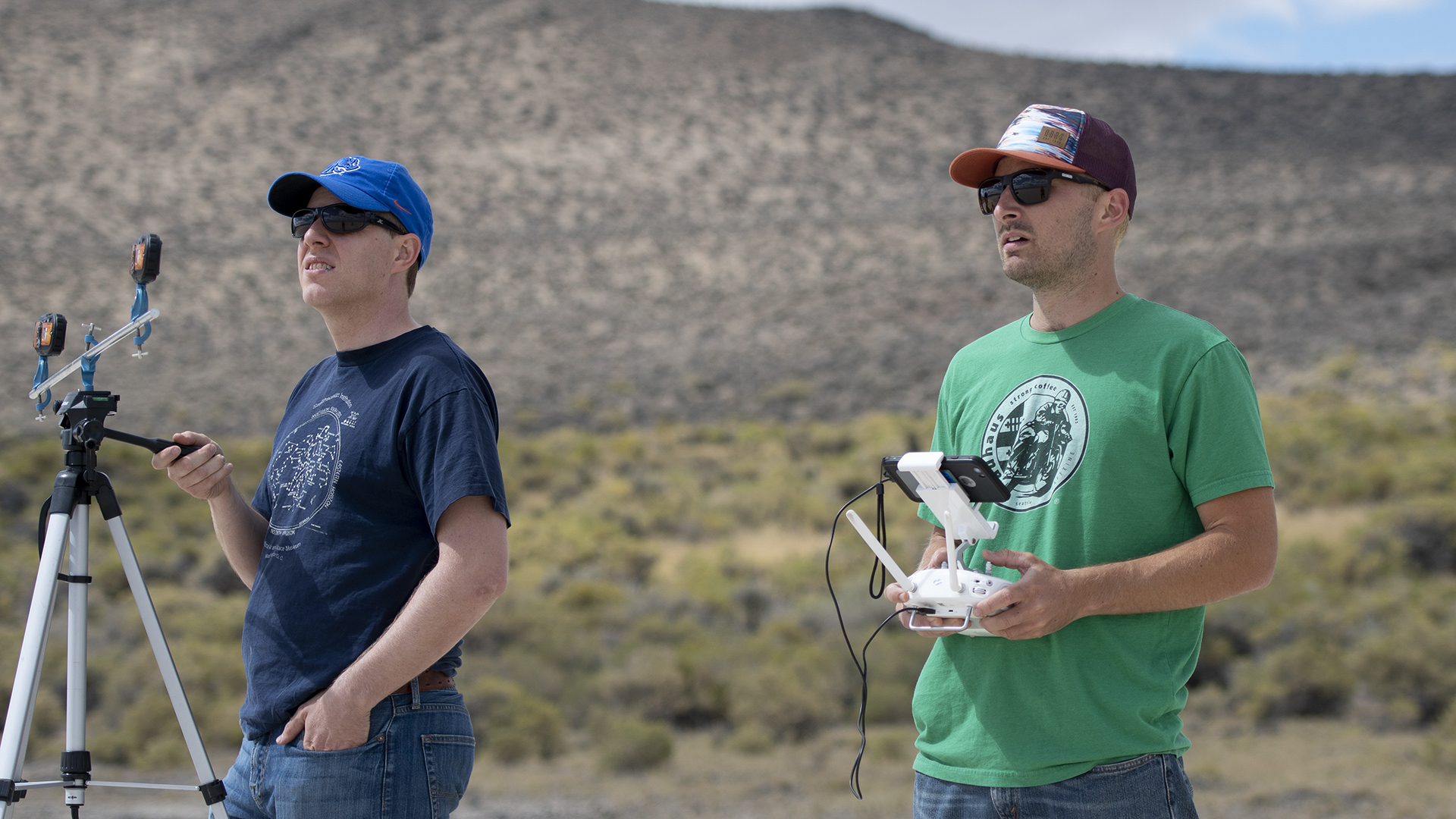 One researcher holding onto tripod, the other one piloting the drone with a controller