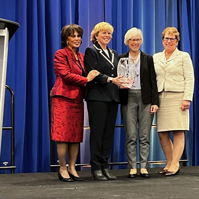 Three women stand next to Cynthia Clark, who holds a glass sculpture award.
