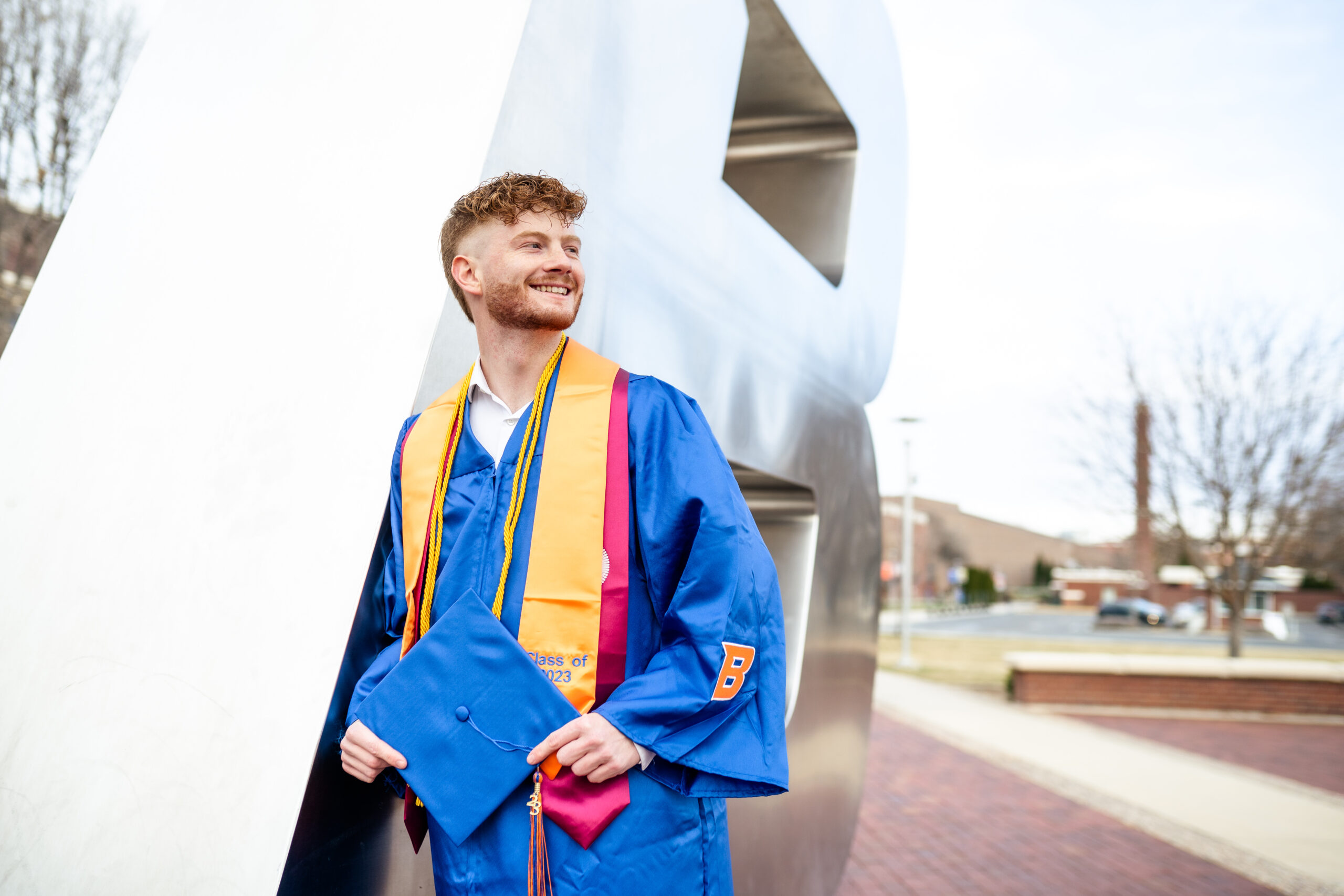Zack Tyree, wearing his commencement regalia, poses in front of the "B" on campus.