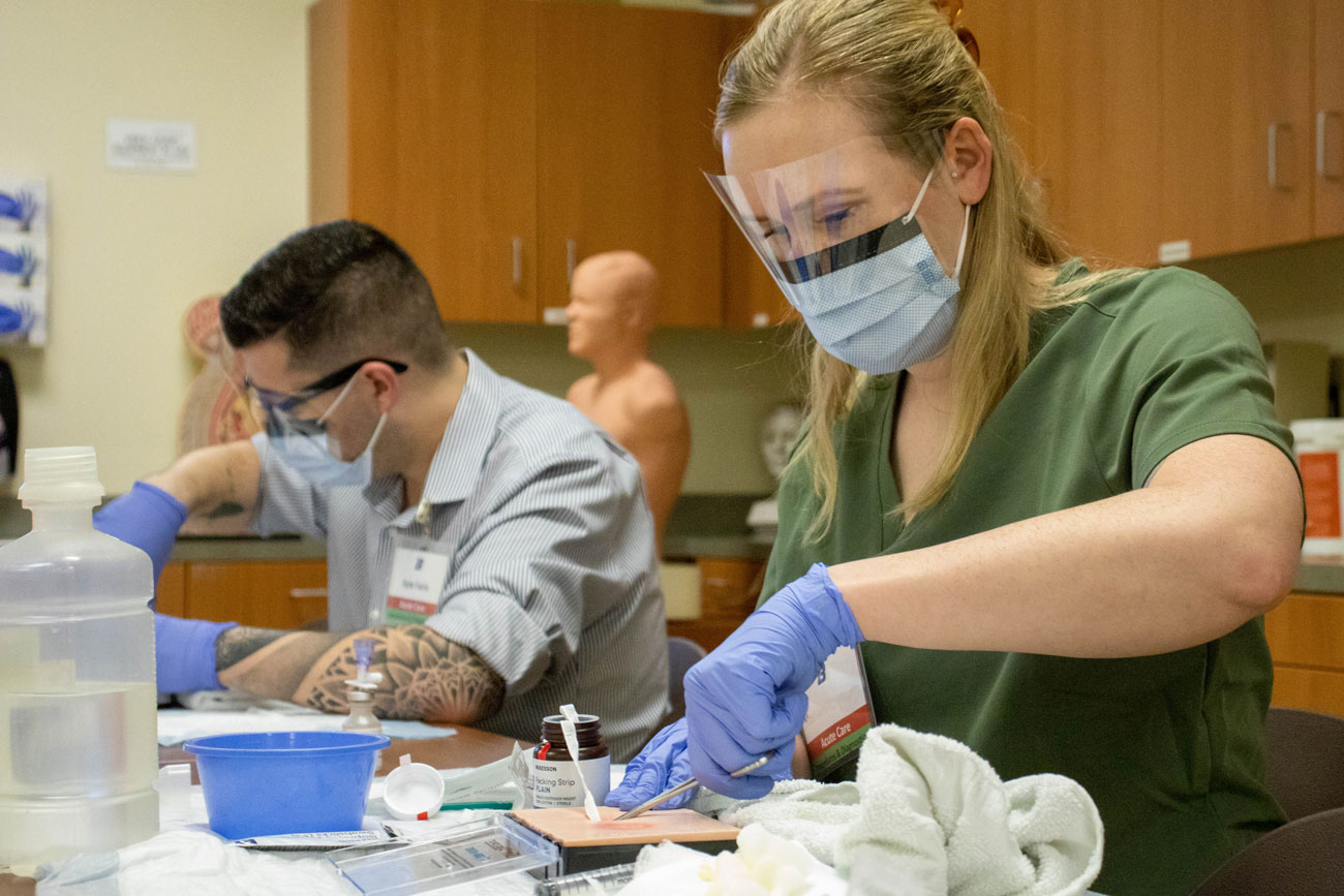 Two nurse practitioner students wear PPE and use scalpels during a practice session.