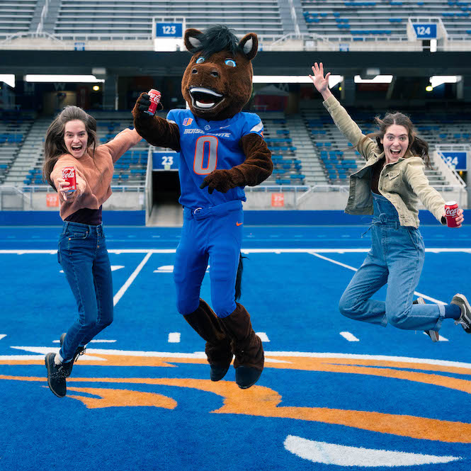 Buster Bronco and fans jump in air on blue turf