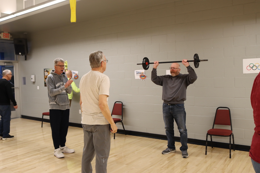 older man demonstrates for two onlookers the proper way to lift a barbell