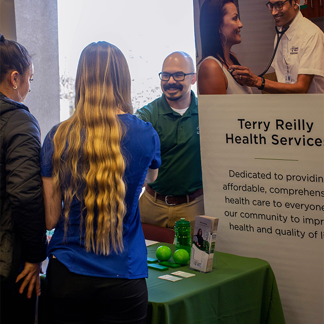Terry Reilly representative talks to two nursing students at a career fair booth.