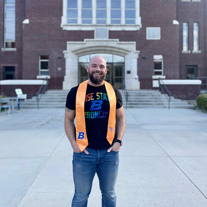 Chris Hughes wears a Boise State t-shirt and stands smiling with his apricot nursing stole.