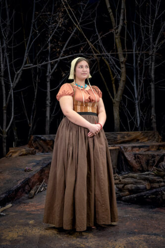 woman in Puritan dress stands on a stage