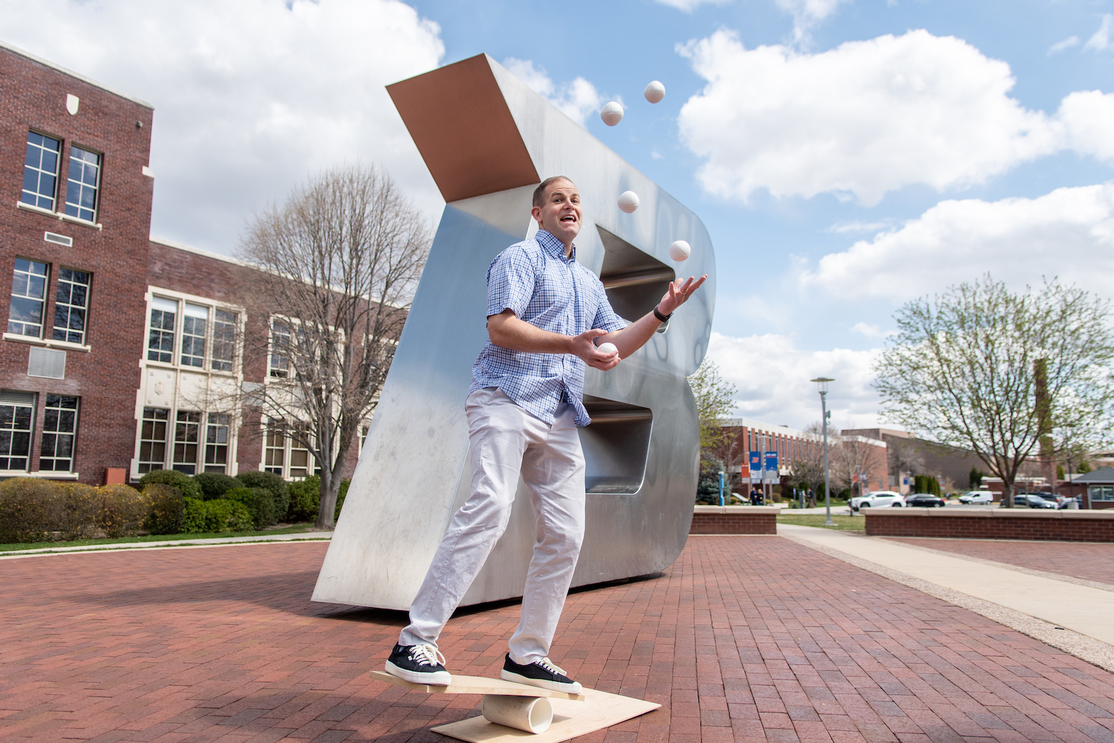 man juggles three balls in front of 'B' statue on campus