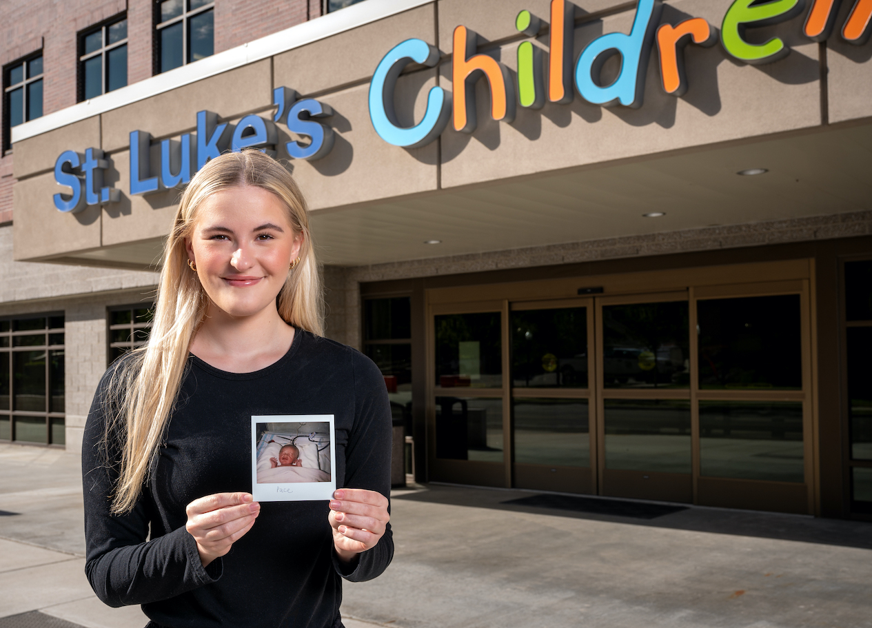woman stands outside St Lukes Hospital holding a polaroid photo of herself as a NICU baby