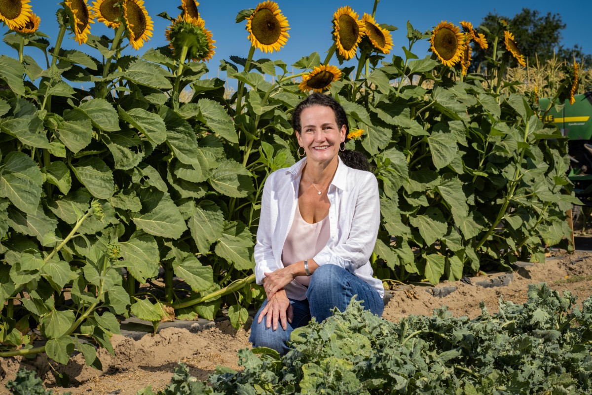 Lindsey Turner kneeling in front of a sunflower field.