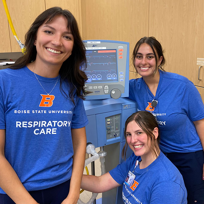 Three respiratory care students pose with a ventilator after helping train Full Circle Health medical students in the respiratory care lab at Boise State.
