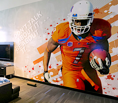 A wall is decorated with a Boise State Football player running and text that says Don't talk about it, be about it