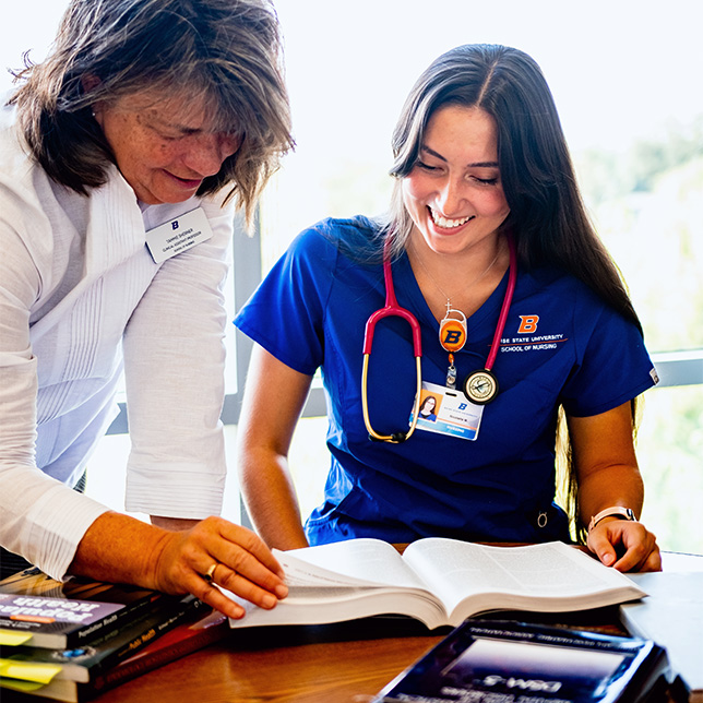 A nursing student smiles as a professor shows her something in a textbook.
