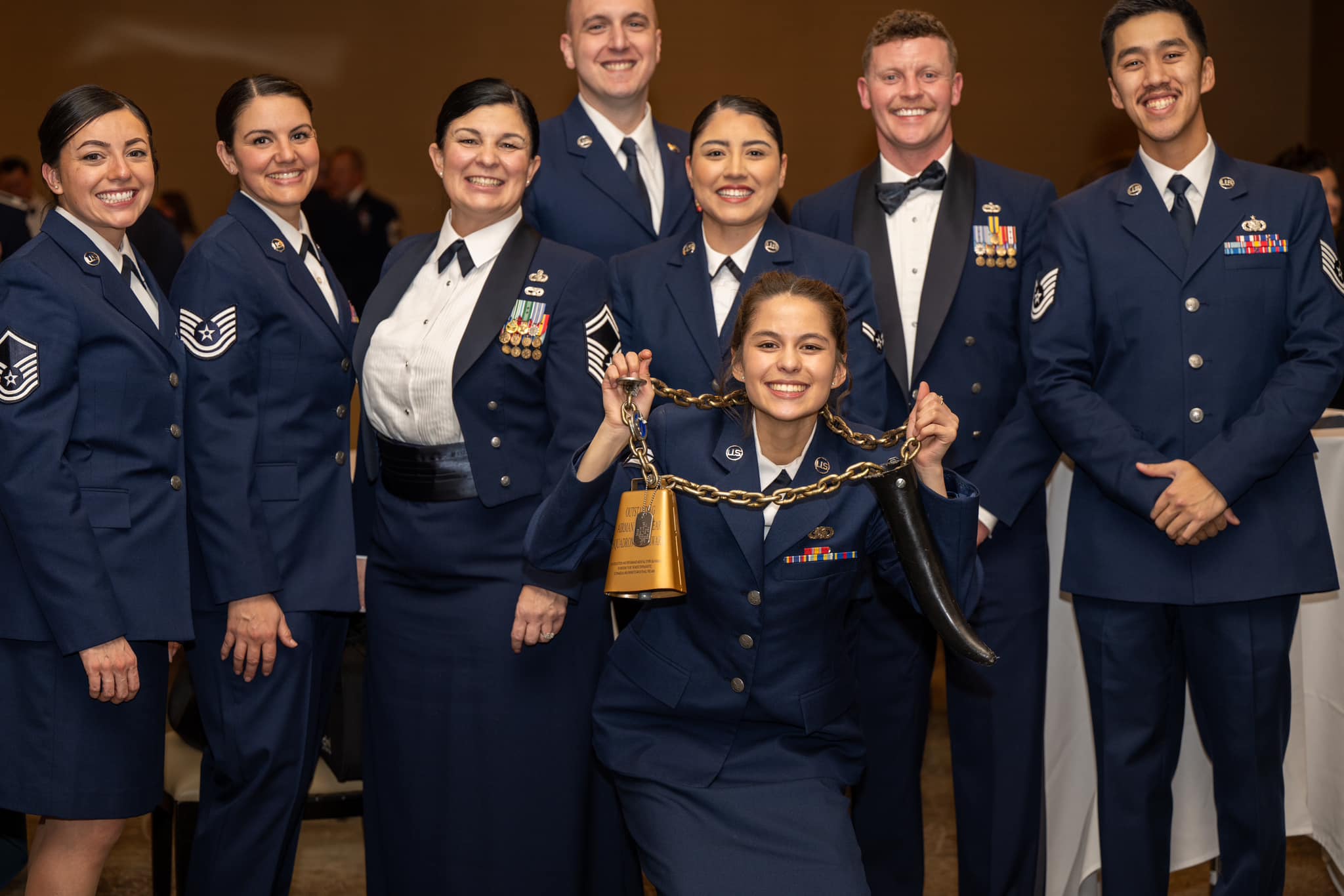 Escarzaga holds a large bell-like award and smiles with seven other airmen in dress uniform.