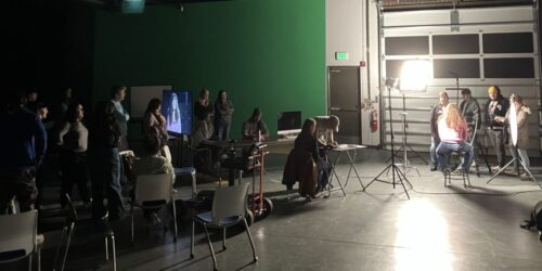 Students filming an interview in a studio. The interviewer and subject are brightly lit.