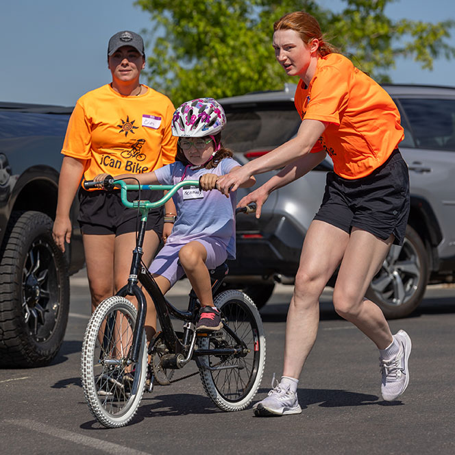 Two Idaho State occupational therapy students aid a young girl with Down syndrome on a bike