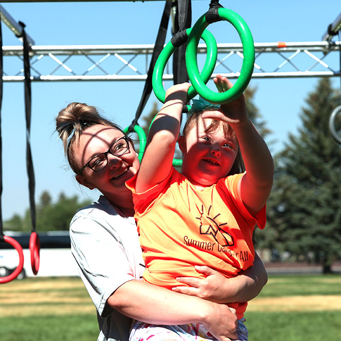 An Idaho State occupational therapy student holds a child with Down syndrome while the child plays on hanging hoops on a playground