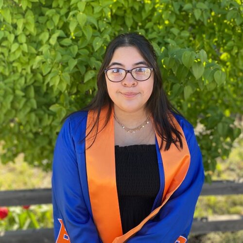 A photo of Emily Muro dressed for Boise State graduation with a nature background.