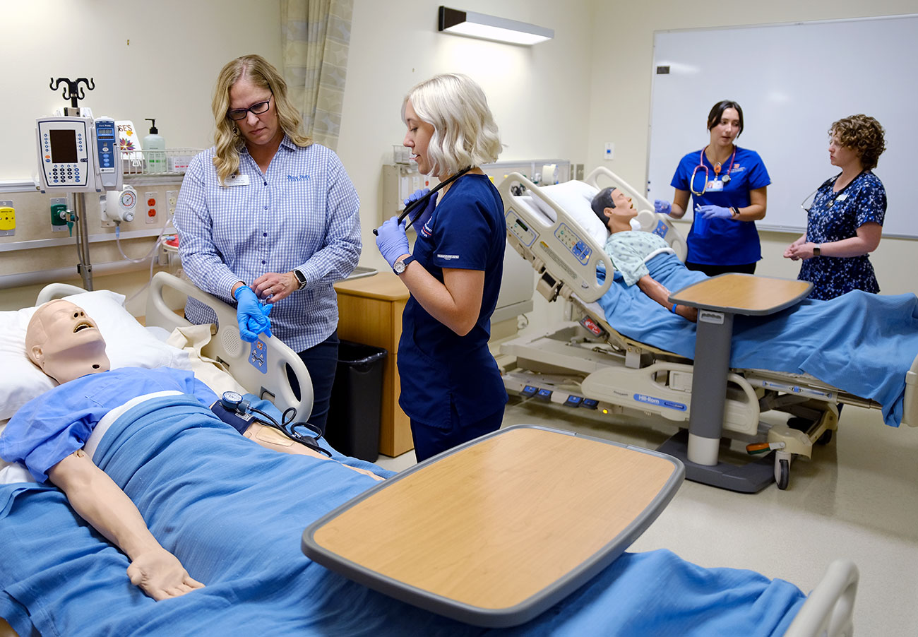 Students and faculty work with two manikins in mock hospital setting