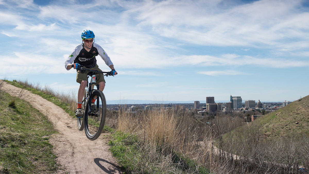 person riding mountain bike on trail, downtown Boise in the background