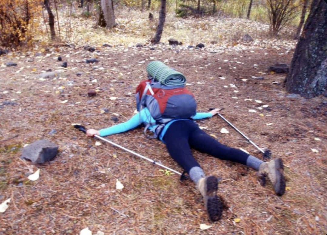 Student with hiking gear laying face down on the forest floor in exhaustion