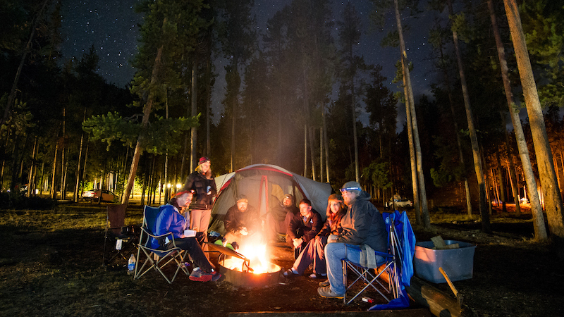 students sit around a tent and campfire at night