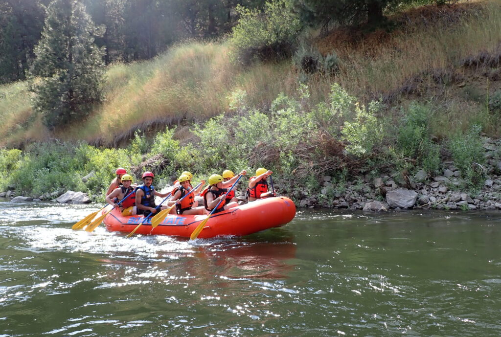 Group of students in raft paddling down the river
