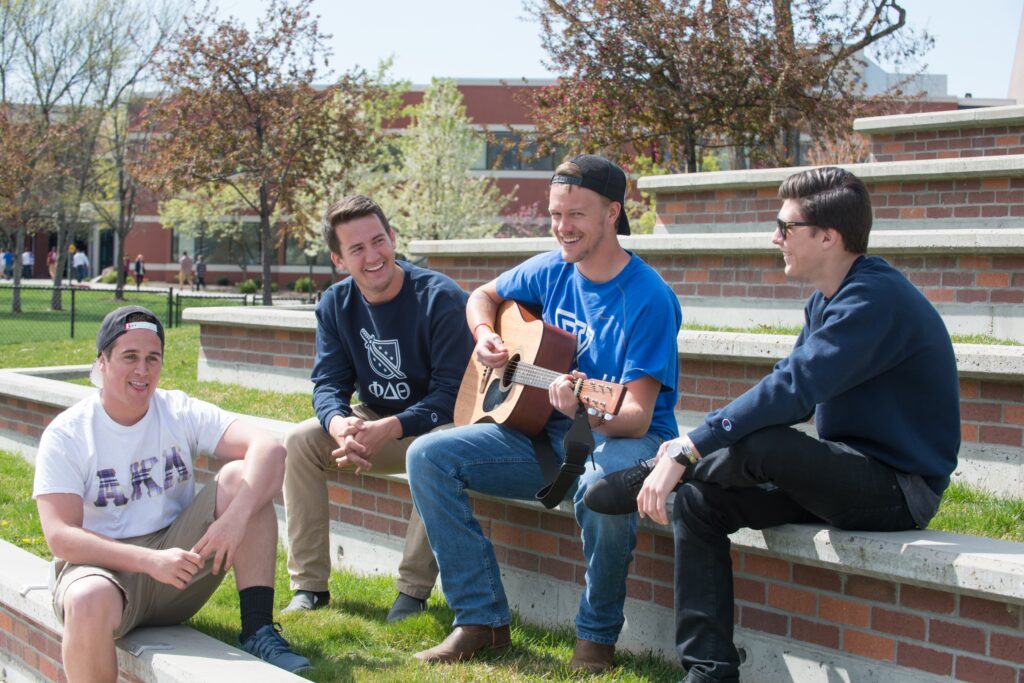 Students from Greek Life gather to enjoy music being played on a guitar.