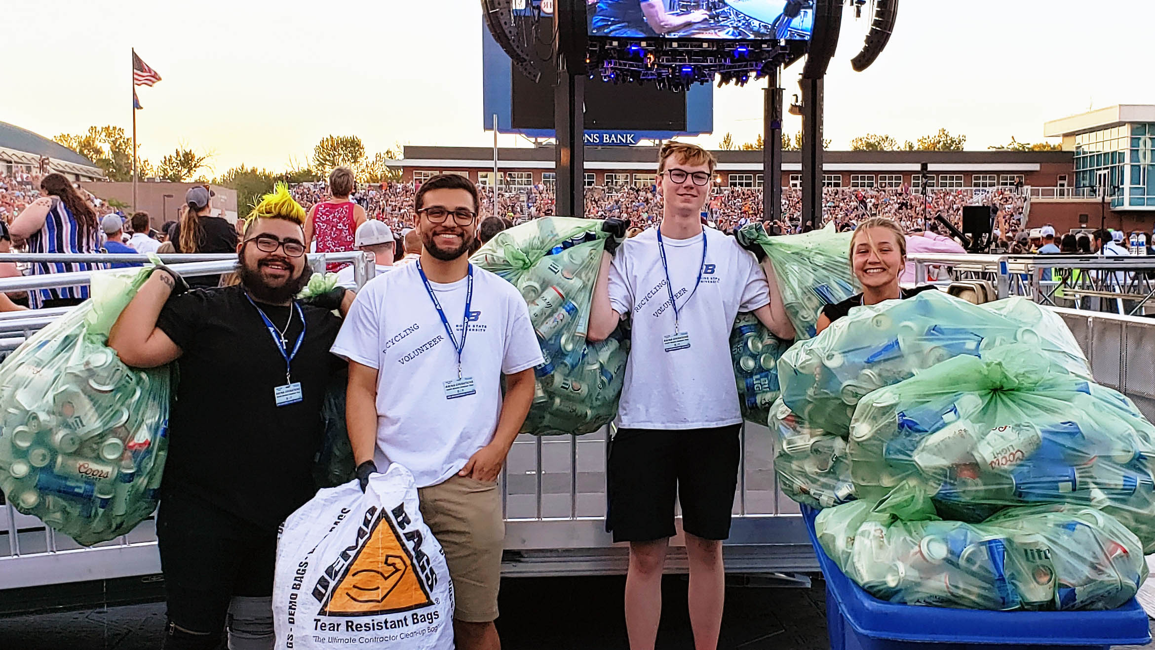 A group of students smiling and carrying large bags of cans to recycle