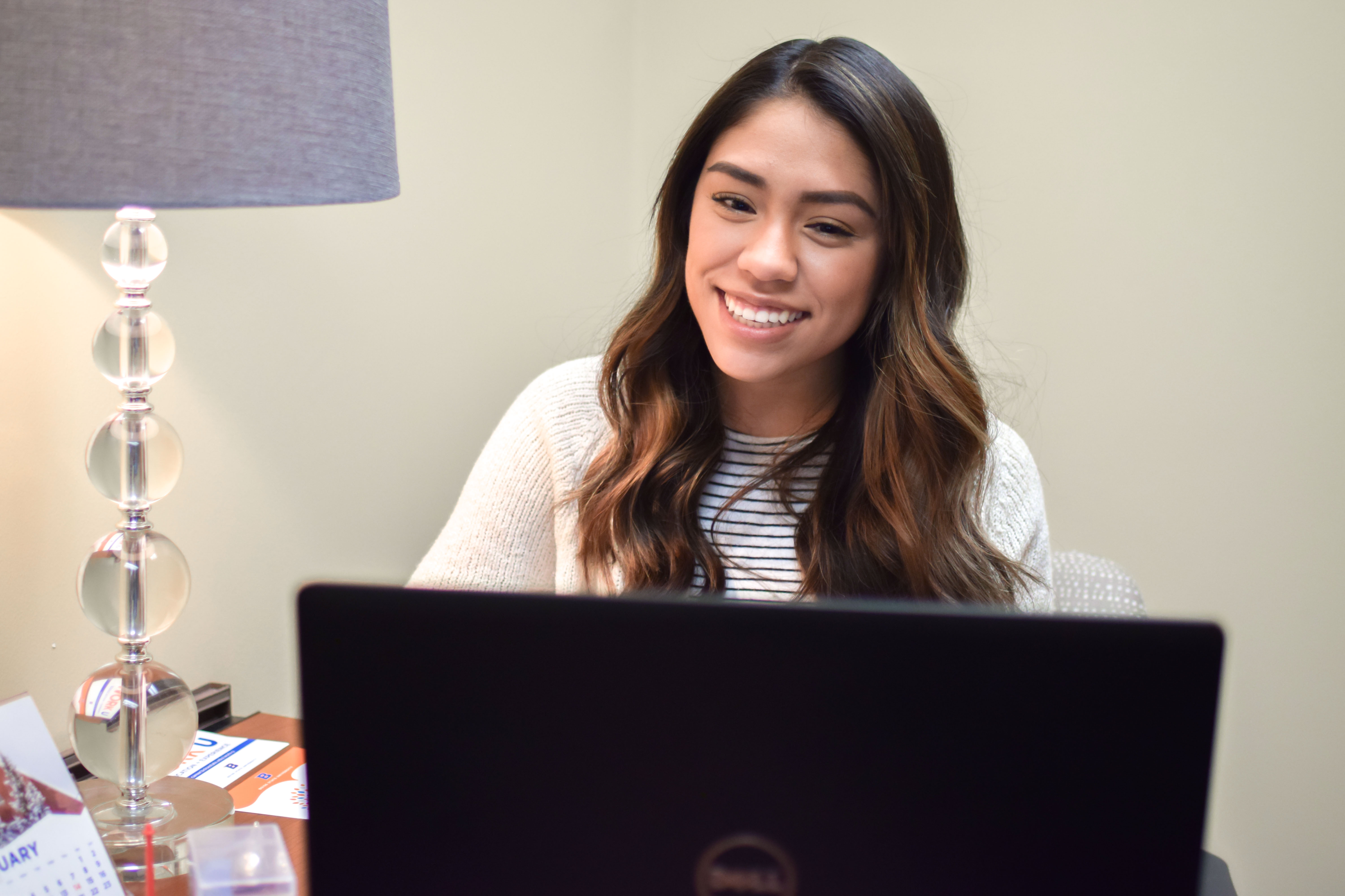 Student looking at laptop and smiling, participating in an online video appointment with a career counselor