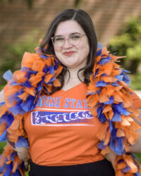 Paige McMahon posing in a Boise State t-shirt and a blue and orange boa