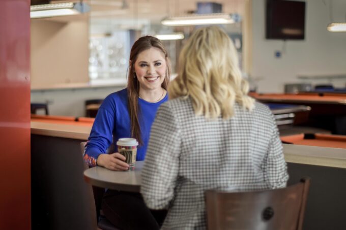 Student and employer sitting across a table smiling at each other during an informational interview