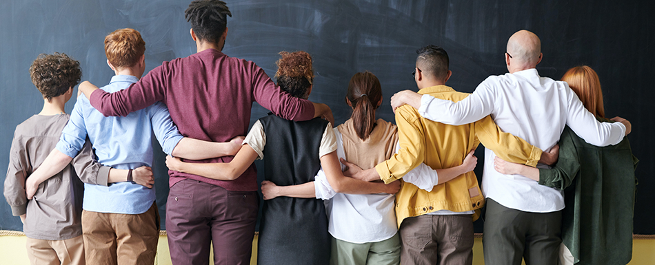 Group of people facing a chalkboard, their arms around each other